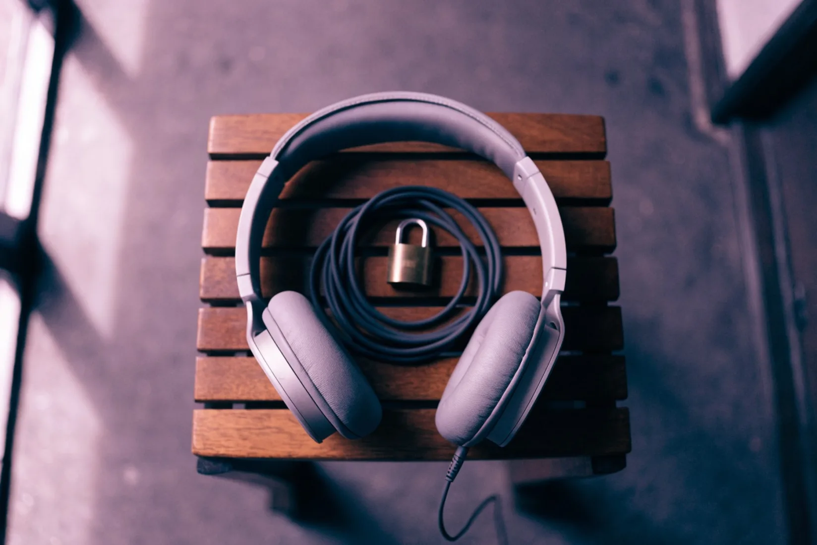 A pair of over-ear headphones lying on a slatted wooden gym bench, photographed from above, with a small brass padlock resting on the coiled cable.